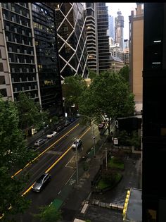 a city street filled with lots of traffic next to tall buildings and green trees on both sides