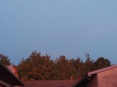 an airplane flying in the sky over rooftops with trees and buildings behind it at dusk