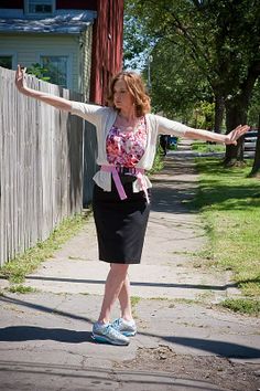 a woman is standing on the sidewalk with her arms out and she's wearing a skirt