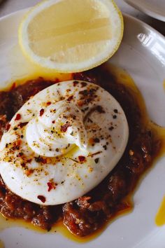 a white plate topped with an egg covered in sauce next to a slice of lemon