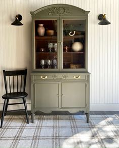 a green china cabinet sitting next to a black chair on top of a carpeted floor