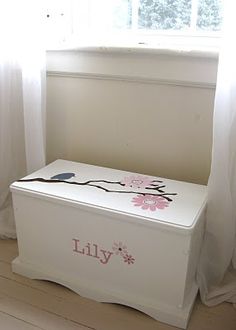 a white toy box with pink flowers on it in front of a window and curtains