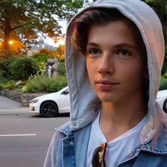 a young man wearing a hoodie standing in front of a street with parked cars