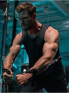 a man with muscular arms and legs working on his muscles in a gym area, holding a pair of scissors