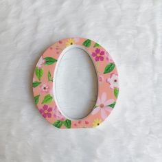 a pink and green flowered oval shaped mirror on a white furnishing area