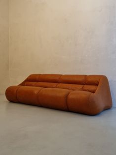 an orange leather couch sitting on top of a cement floor next to a white wall