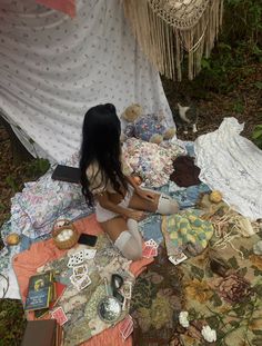 a woman sitting on the ground next to a pile of cloths and other items