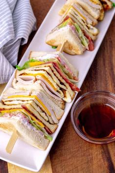 a long white plate topped with sandwiches next to a cup of tea on top of a wooden table