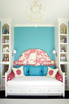 a bedroom with blue walls and a pink headboard on the bed in front of a white bookcase