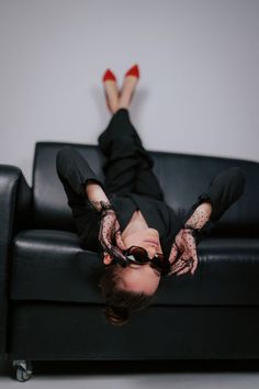 a woman laying on top of a black couch with her legs up in the air