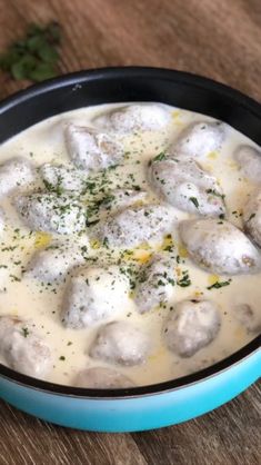 a blue bowl filled with meatballs covered in cheese and sauce on top of a wooden table