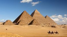 three pyramids in the desert under a blue sky with white clouds and some people