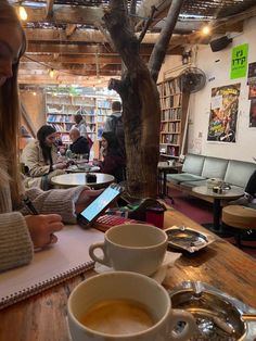 a woman sitting at a table with a cup of coffee in front of her and people working on their laptops