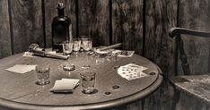 a table with glasses and bottles on it next to a wooden chair in front of a wood paneled wall