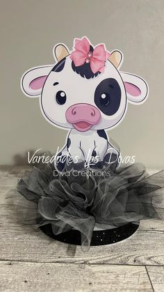 a little cow with a pink bow sitting on top of a wooden floor next to a black and white wall