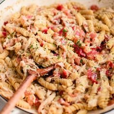 a pan filled with pasta and meat on top of a stove next to a wooden spoon