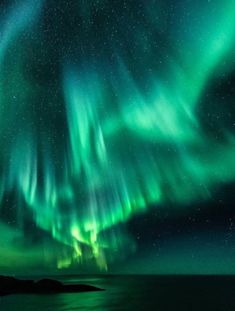 an aurora bore is seen in the night sky over water and land, with bright green lights