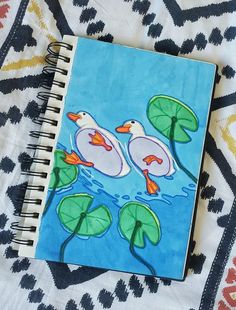 a notebook with two ducks floating on water and lily pads