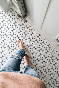 a person standing on the floor in front of a tiled wall and door with their feet up