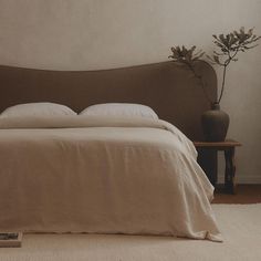 a bed with white sheets and pillows in a room next to a vase filled with flowers