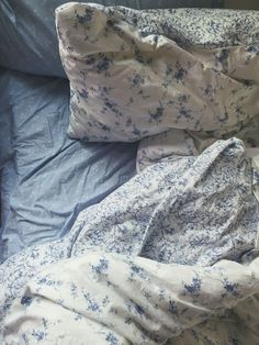 an unmade bed with blue and white comforter on it's side, next to a pillow