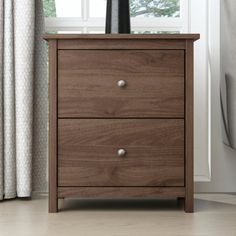 a wooden nightstand with two drawers in front of a window and curtains on the side