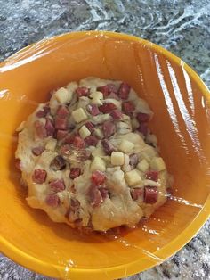 an orange bowl filled with food sitting on top of a marble countertop covered in plastic