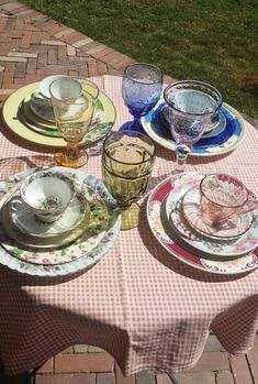 a table with plates and cups on it in front of a brick patio area that has grass