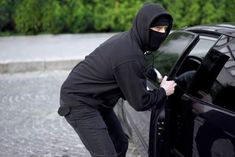 a man in a black hoodie opens the door of a car