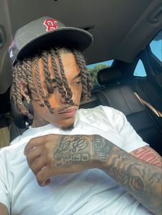 a man with dreadlocks sitting in the back seat of a car wearing a hat