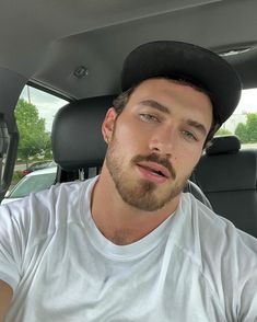 a man sitting in the back seat of a car wearing a black hat and white t - shirt