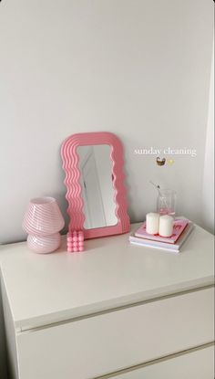 a white dresser with a pink mirror and candles on it, next to a candle holder