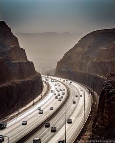 cars are driving down the highway in front of large rocks and mountains on a cloudy day