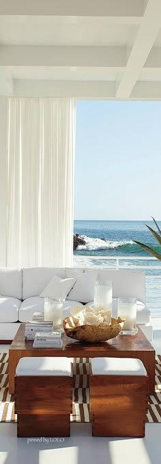 a living room filled with white furniture and an ocean view behind the couch is a coffee table