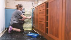 a woman in grey shirt and black shorts kneeling on the floor next to wooden cabinets