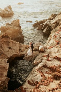 a bride and groom standing on rocks near the ocean