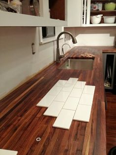 a kitchen counter top with white tiles on it and wood flooring in the background