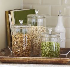 three glass jars filled with food on top of a wooden tray next to a book