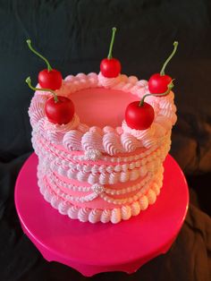 a pink cake with white icing and cherries on top