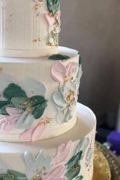 a three tiered wedding cake with flowers painted on the side and gold trimmings