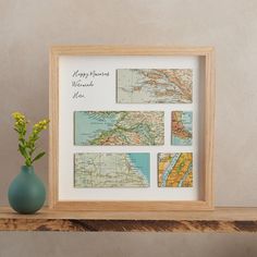 a vase with flowers sitting on top of a wooden shelf next to a framed map