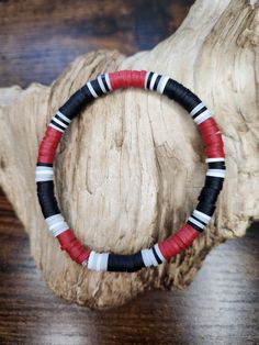 a red, white and black beaded bracelet sitting on top of a wooden table