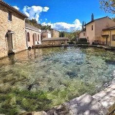 an outdoor swimming pool with clear water and stone buildings in the background, surrounded by greenery