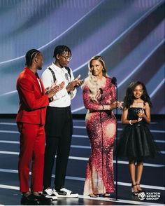 three people standing on stage with one holding a microphone and the other wearing a red suit