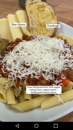 a white plate topped with pasta covered in sauce and cheese next to a slice of bread