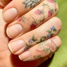 a woman's hand with tattoos on it and flowers painted on the ring finger