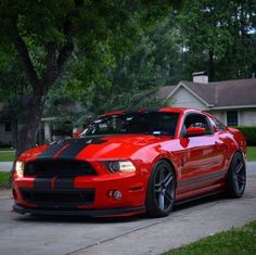 a red and black mustang parked on the side of a road in front of a house