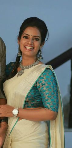 a smiling woman in a white sari holding onto her arm and looking at the camera