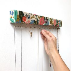 a hand is holding a necklace holder on the wall