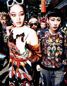 two young women standing next to each other in front of a group of people on the street